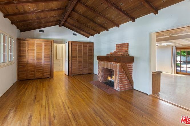 Living room with wood floor, beam ceiling, brick fireplace, and wood cabinets
