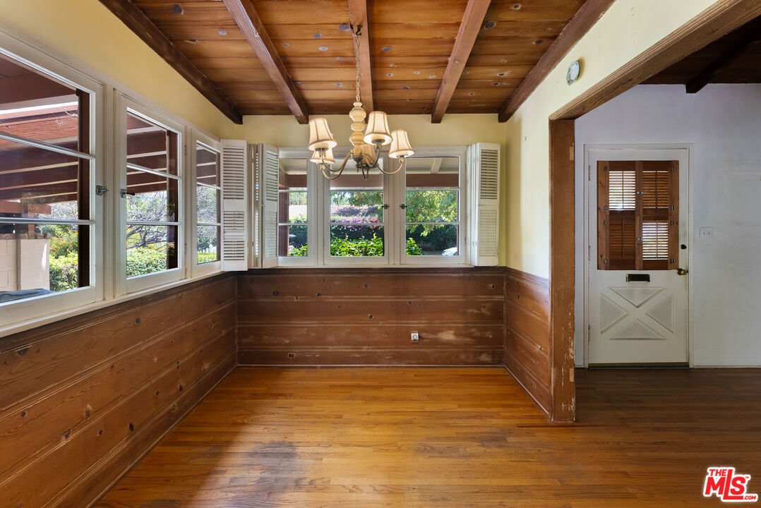 Room with wood walls, beam ceiling, chandelier, windows with shutters, and door