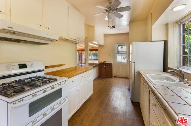 Kitchen with gas stove, white cabinets, sink, fridge, and wood floor