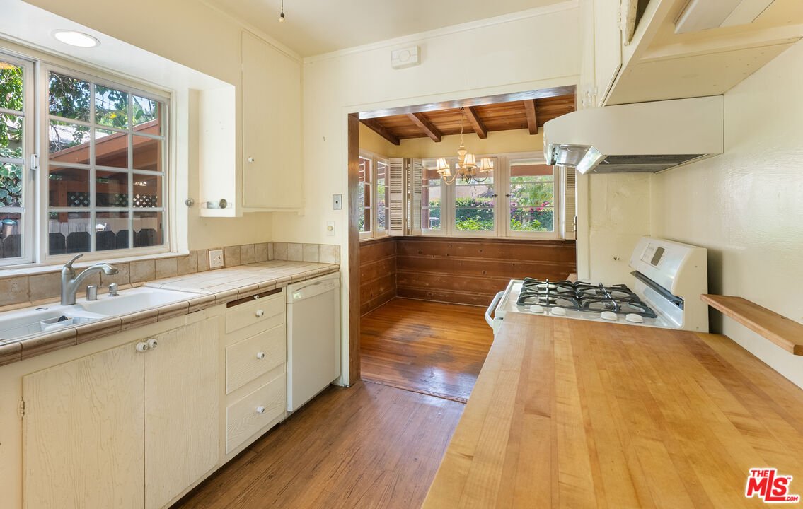 Kitchen with white cabinets, wood counter, gas stove, and window