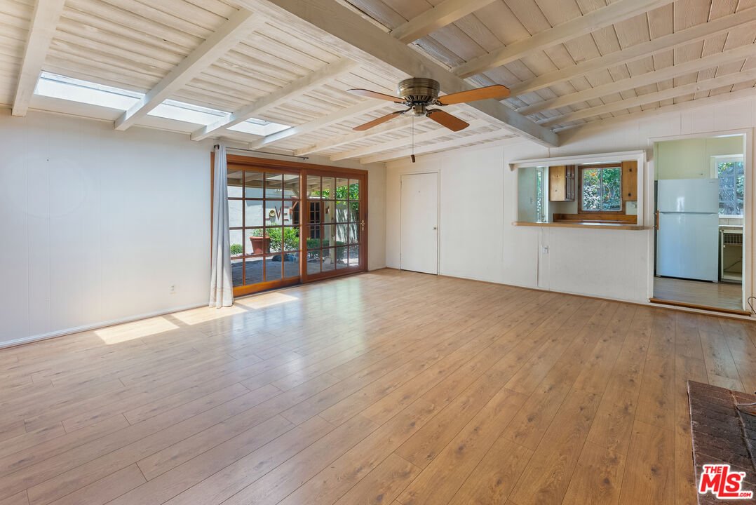 Room with wood floor, fan, big windows, and open kitchenette