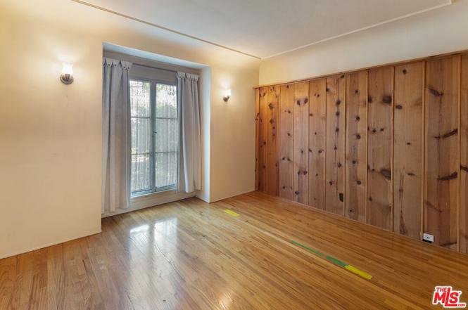Room with wood floor, wood wall panels, window with curtains, and door to patio