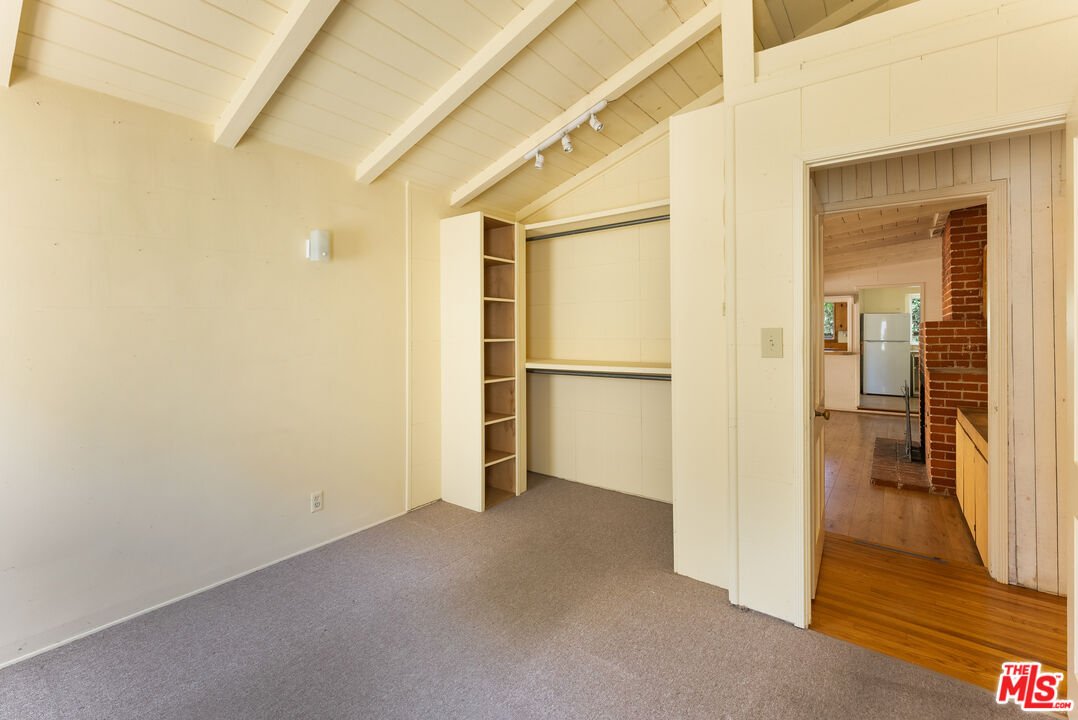 Room with sloped ceiling, carpet floor, shelves, and doorway