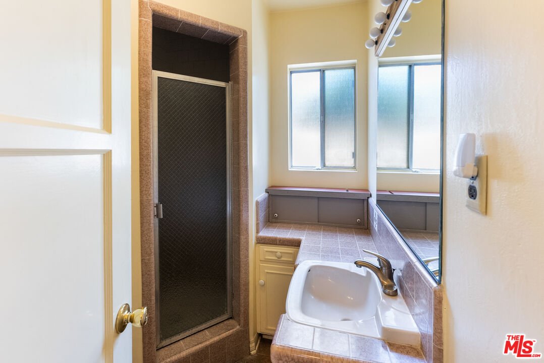 Bathroom with shower, sink, windows, and tile walls