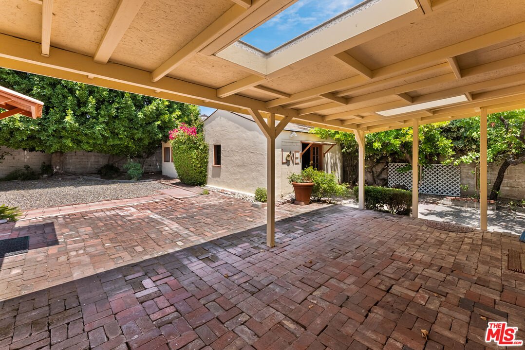 Backyard with brick floor, green plants, and two buildings in background