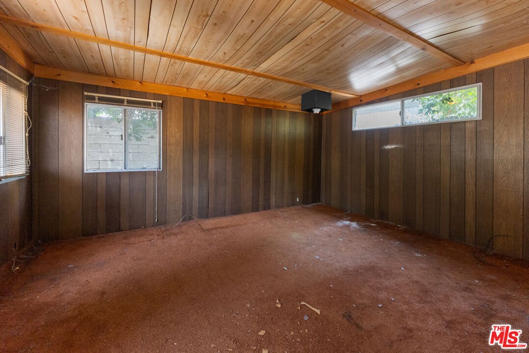 Room with wood panels, shelves, fridge, window, and unfinished floor