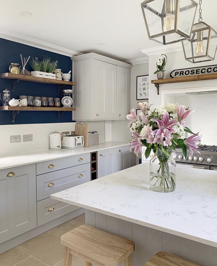 Kitchen with grey cabinets, marble counter, shelves, oven, and pink lilies.