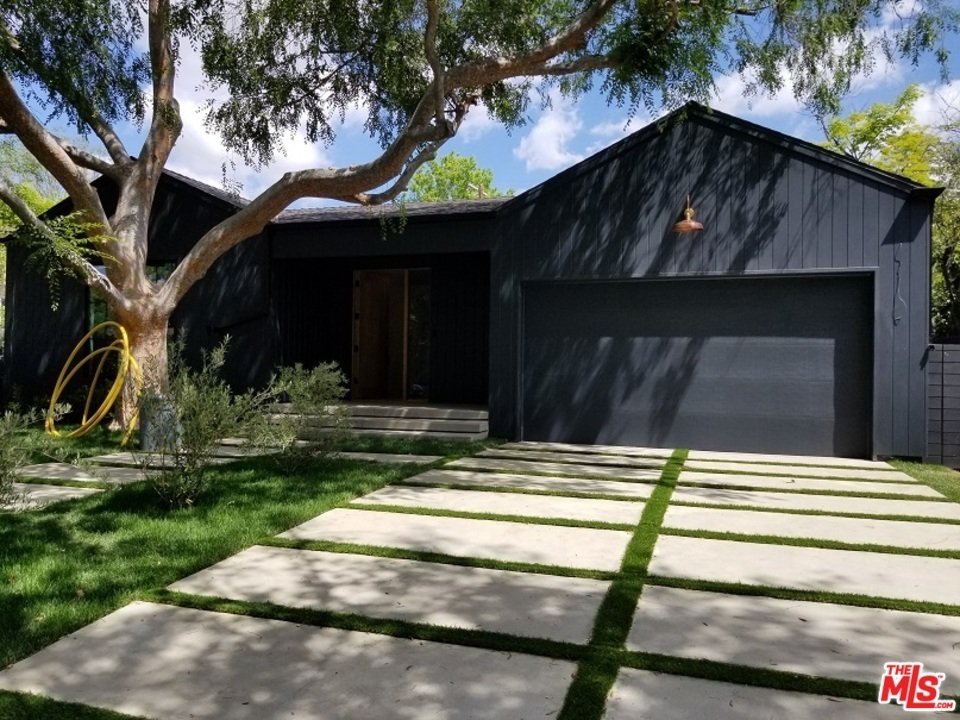 Luxury black house with large yard, concrete path, and garage, California real estate.