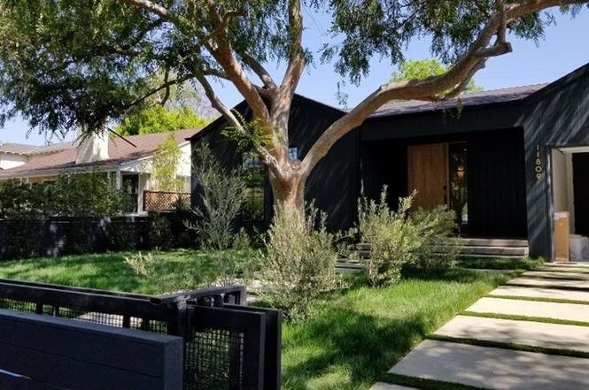 Luxury black house with wooden door, green lawn, and trees.