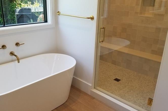 Bathroom with white bathtub, glass shower, and gold towel bar.