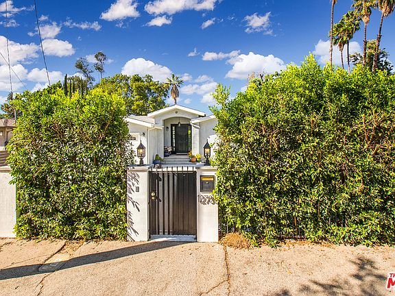 California real estate home with tall bushes, black gate, and front yard.