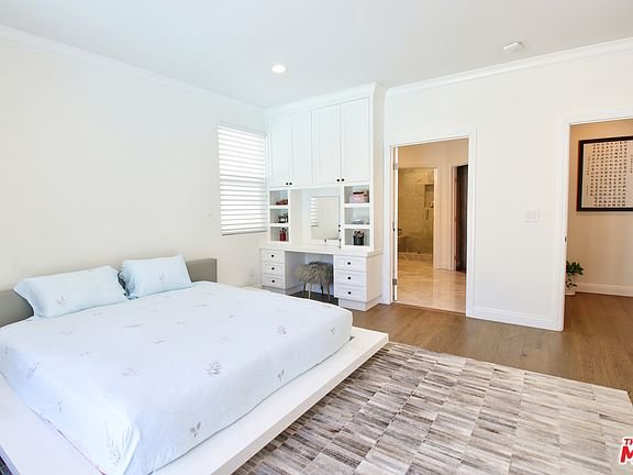 Bedroom with bed, rug, built-in desk, shelves, and open doorway.