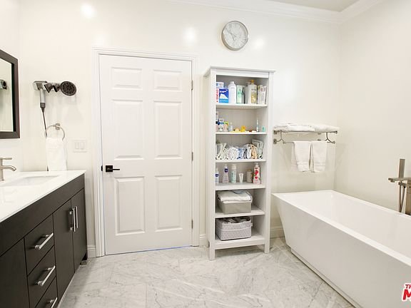 Bathroom with bathtub, double sink vanity, shelf, towel rack, and clock.