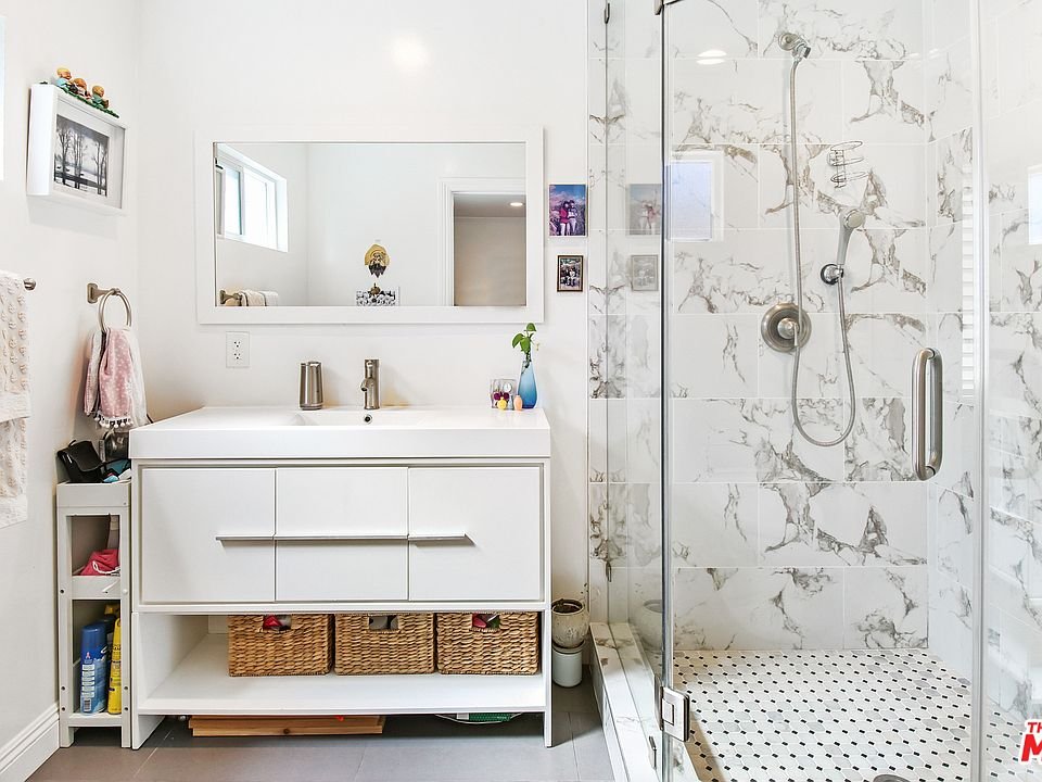 Bathroom with double sink vanity, mirror, glass shower, and baskets.