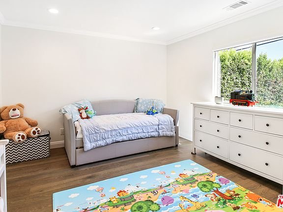 Kids bedroom with daybed, dresser, play rug, teddy bear, and window.