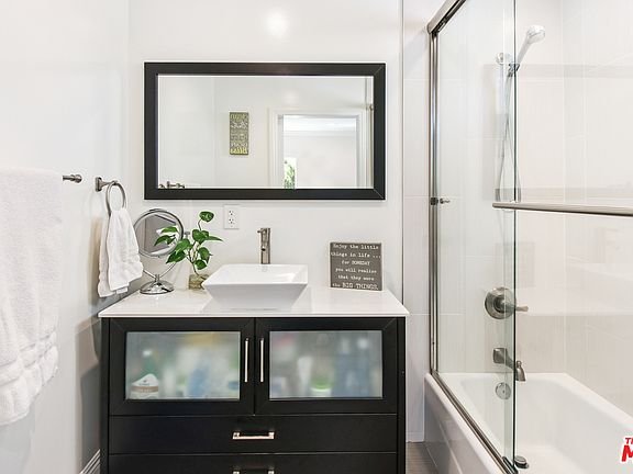Bathroom with sink vanity, mirror, glass shower, and plant.
