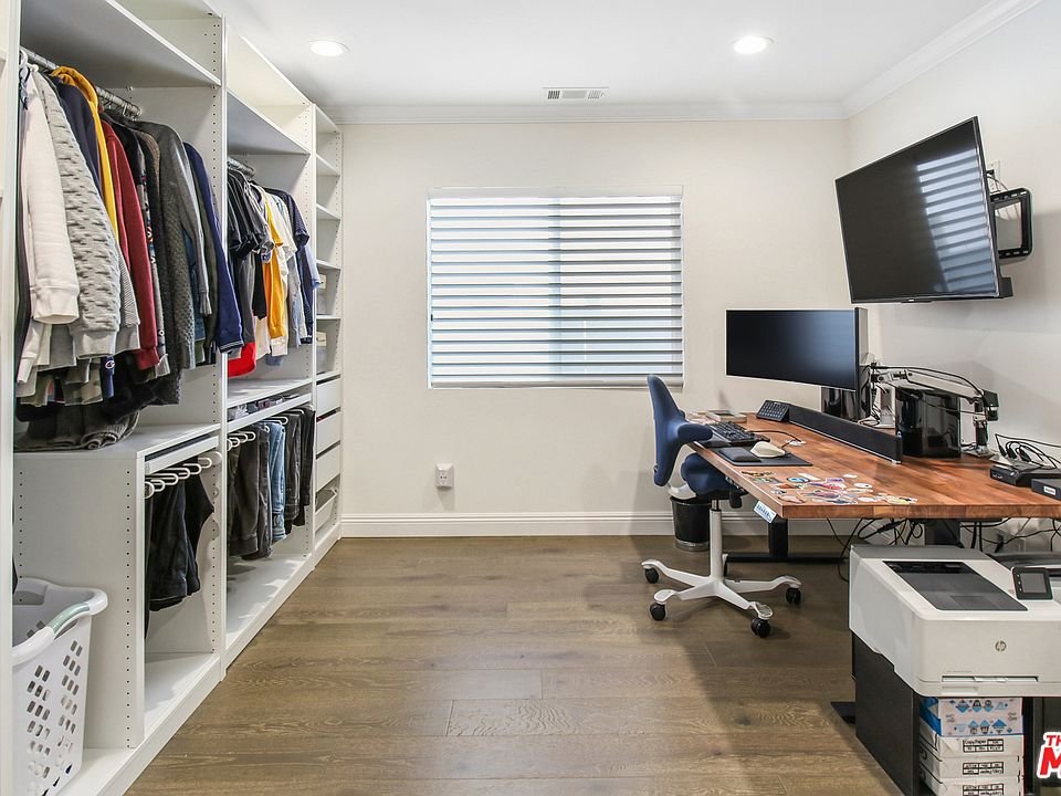Room with closet shelves, clothes, desk, monitors, and printer.