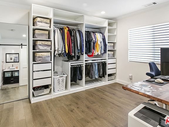 Bedroom closet with clothes, drawers, bins, desk, and mirror.