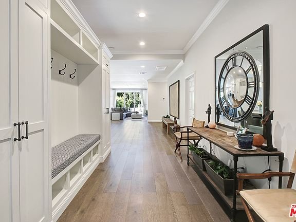Hallway with bench, wall hooks, round mirror, table, and plants.