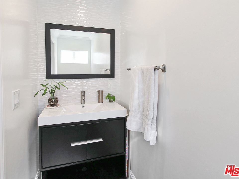 Bathroom with black vanity, mirror, towel rack, plant, and tile wall.