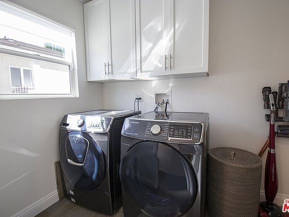 Laundry room with washer, dryer, cabinets, window, and basket.