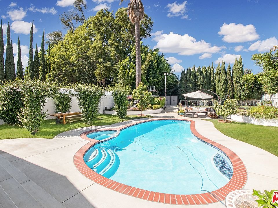 Backyard pool with grass, plants, and trees in California real estate.