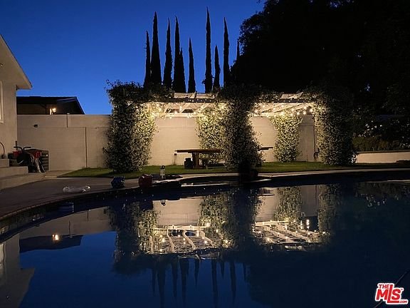 Backyard pool with pergola, lights, trees, and water view.