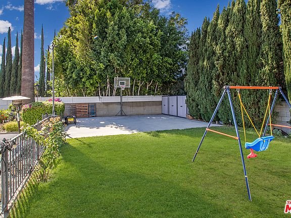 Backyard in California real estate with grass, basketball hoop, swing set, and trees.