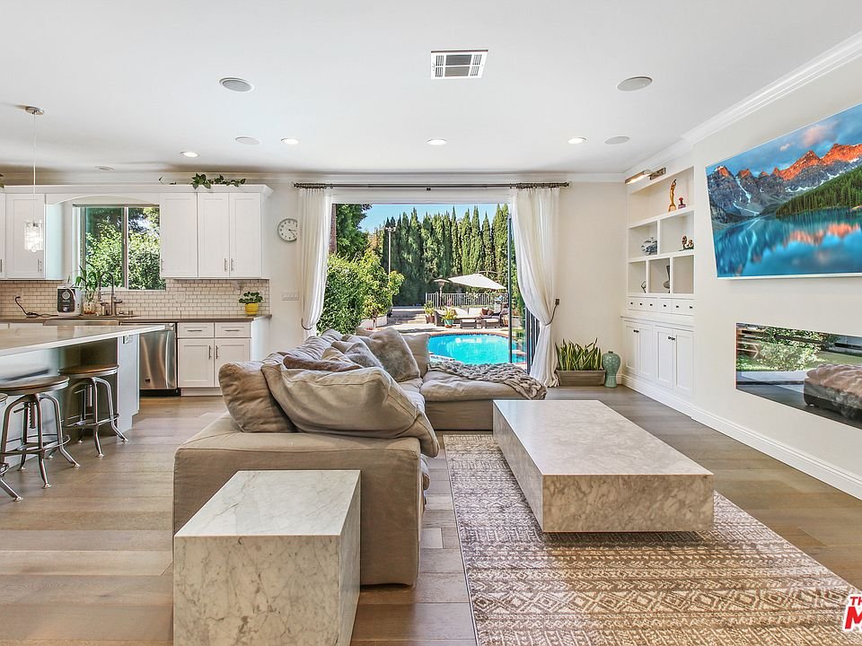 Living room with sofa, marble coffee table, plants, artwork, and windows to pool.