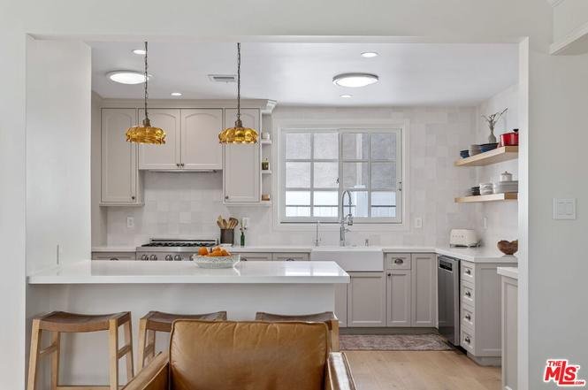 Modern kitchen with light cabinets, large window, countertop, bar stools, and shelves.