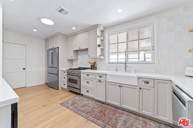 Modern kitchen with gray cabinets, farmhouse sink, stainless steel appliances, and wood floor.