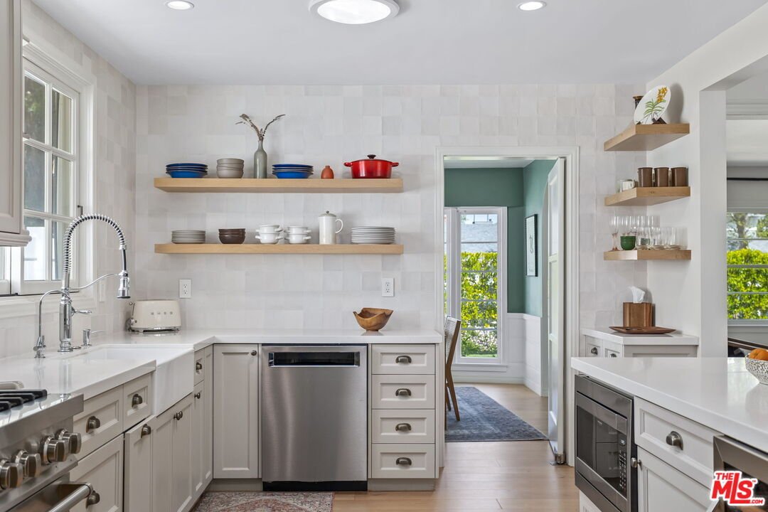 Modern kitchen with white cabinets, stainless steel appliances, open shelves, and door to outdoor area.