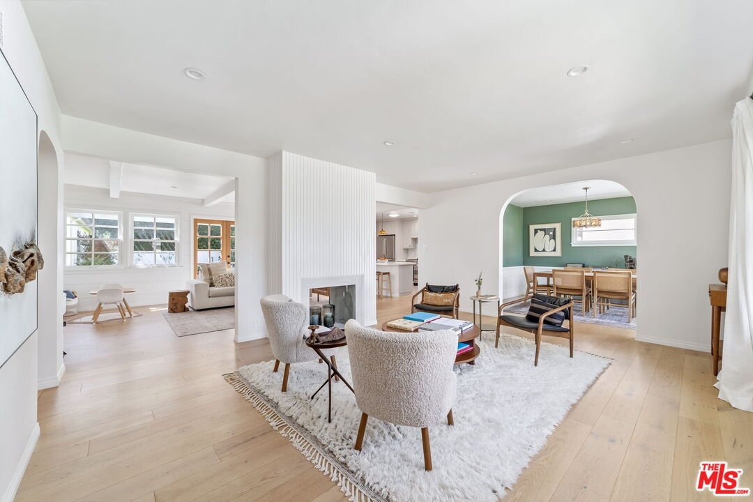Modern living room with wood floor, large rug, chairs, coffee table, wall art, and dining area.