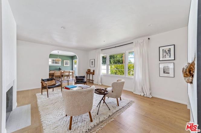 Modern living room with wood floor, rug, chairs, coffee table, wall art, and dining area.