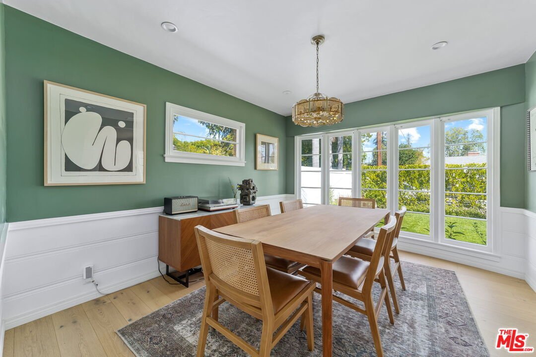 Modern dining room with wooden table, six chairs, green wall, wall art, and large windows.