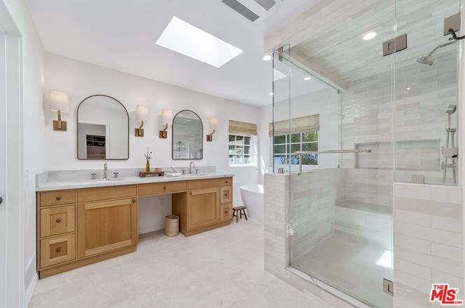 Modern bathroom with double sinks, wood cabinets, mirrors, and glass shower.