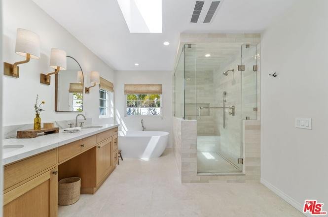 Bathroom with double vanity, round mirror, glass shower, bath tub, and skylight.