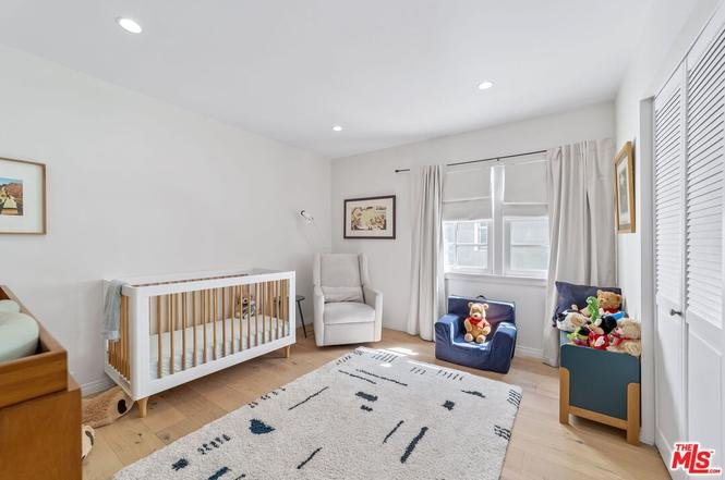 Nursery room with crib, rocking chair, plush toys, wood floor, curtains, and wall art.