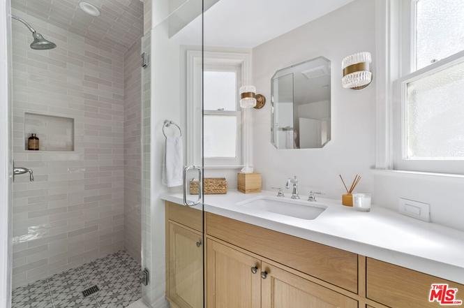 Modern bathroom with glass shower, light tiles, double vanity, marble counter, wood cabinets, and mirror.