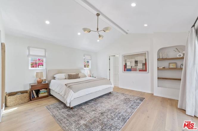 Modern bedroom with large bed, wood floor, windows, wall art, and shelves.