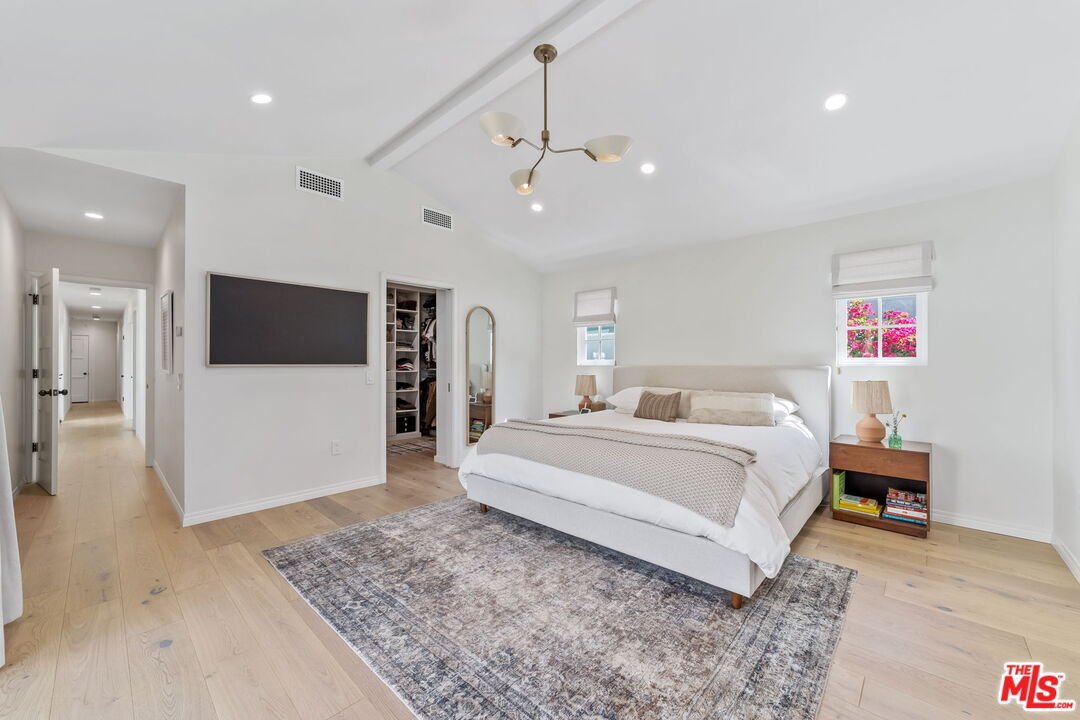 Modern bedroom with large bed, wood floor, rug, TV, window, and doorway.