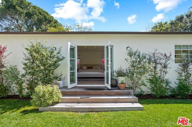 California real estate house with white exterior, wood deck, green lawn, and shrubs.
