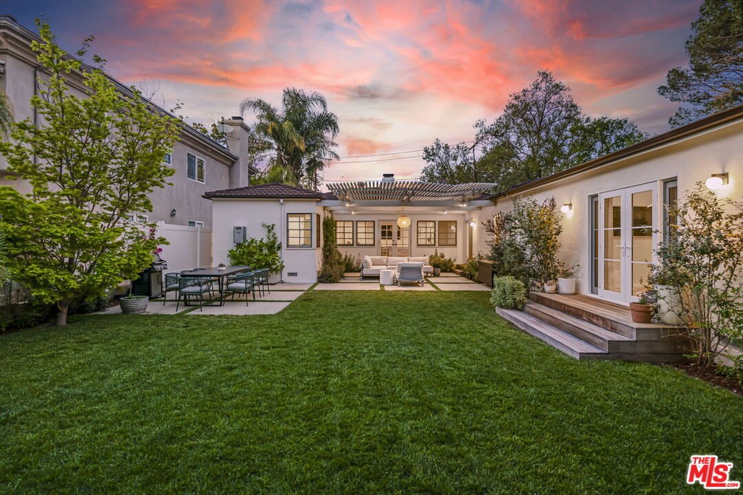 California real estate house backyard with green lawn, patio table, chairs, and trees.