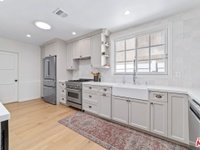 Modern kitchen with light cabinets, stainless steel appliances, large sink, wood floor, and window.