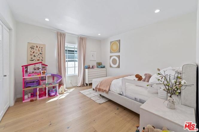 Modern bedroom with white bed, wood floor, plush toy, toy house, and window.