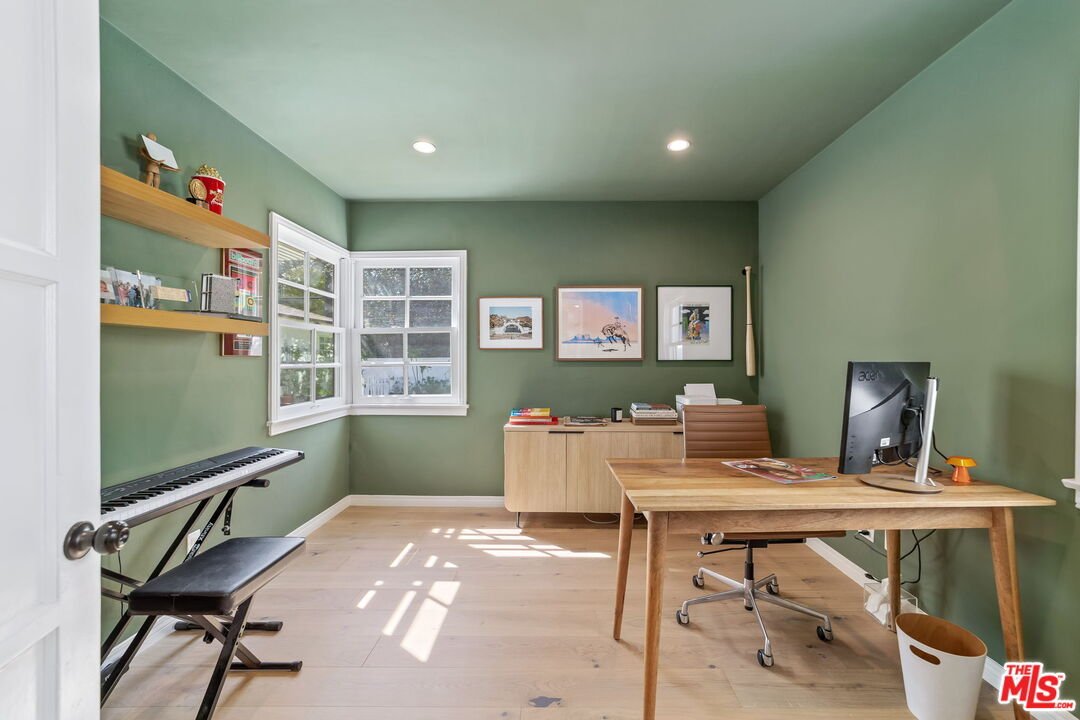 Modern home office with green walls, wooden desk, chair, keyboard, and wall art.