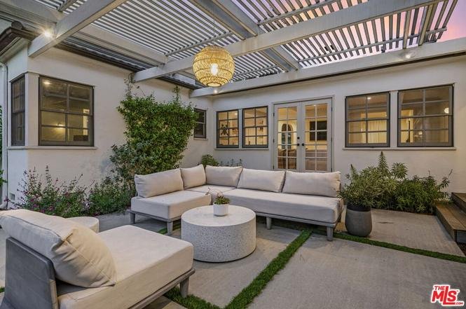 California real estate house patio with sectional sofa, round coffee table, pendant light, and windows.