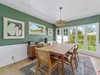 Modern dining room with wooden table, chairs, chandelier, green walls, and large windows.