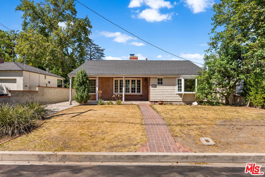 California real estate home with front yard, brick path, trees, and open space.