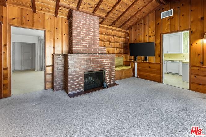 Living room with wooden walls, brick fireplace, and carpeted floor.
